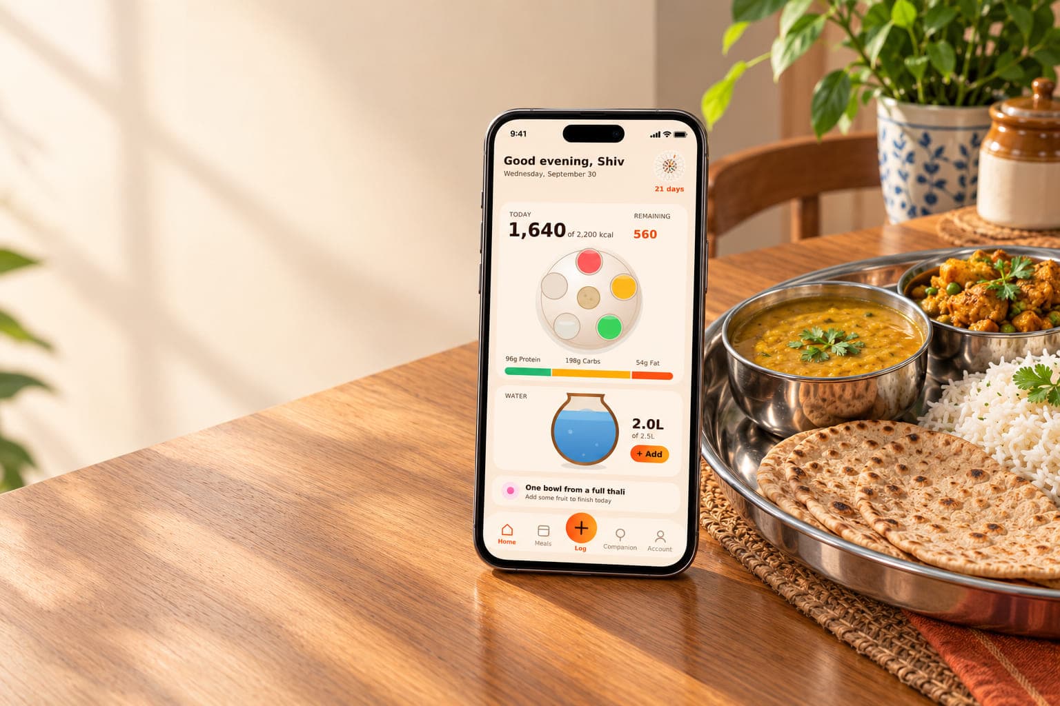 A phone showing the Katori app beside a home cooked Indian thali of dal, sabzi, rice and roti on a sunlit wooden table